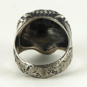 May include: A silver ring with a textured band and a skull design on the top.