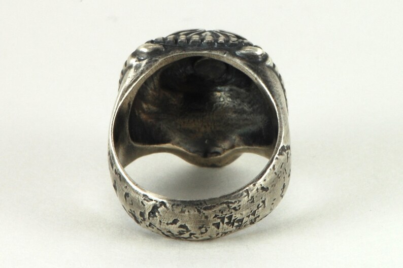 May include: A silver ring with a textured band and a skull design on the top.
