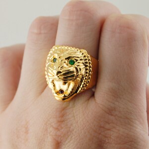 May include: A gold ring with a lion head design. The lion's eyes are green gemstones.