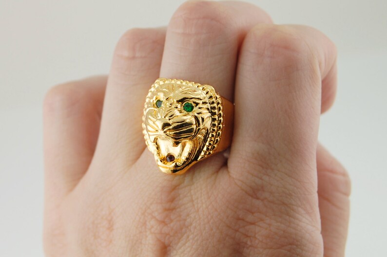 May include: A gold ring with a lion head design. The lion's eyes are green gemstones.