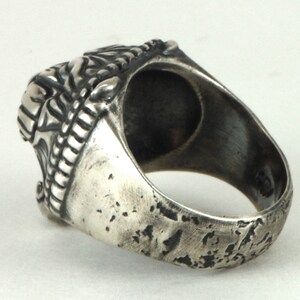 May include: A silver ring with a detailed design on the top and a textured band. The ring is worn and has a distressed look.