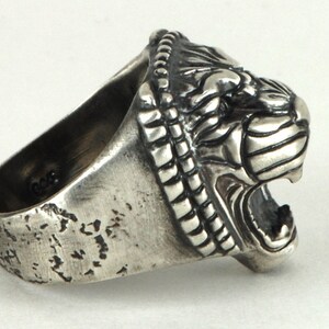 May include: A silver ring with a detailed lion head design. The ring is textured and has a worn look.