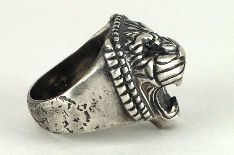May include: A silver ring with a detailed lion head design. The ring is textured and has a worn look.