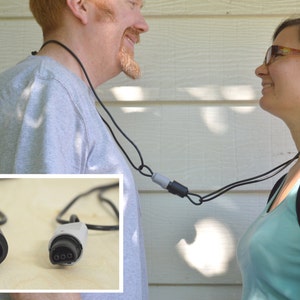 May include: Two people wearing black cords around their necks with a gray and black connector. The cords have a black and a gray connector on the ends.