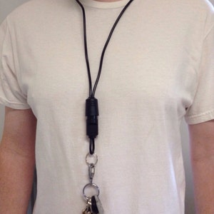 May include: A black lanyard with a black key holder and a set of keys attached. The lanyard is worn around the neck of a person.
