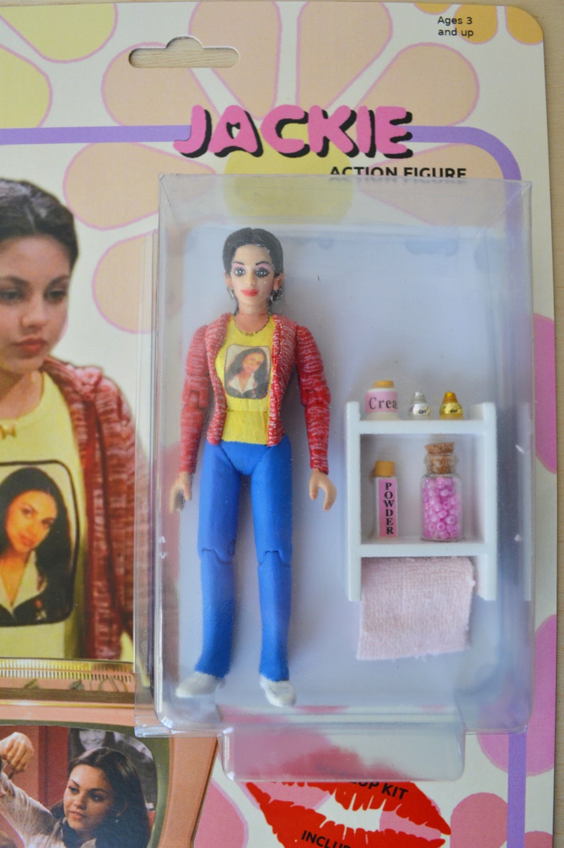 May include: A plastic action figure of a young woman with brown hair and a red and white striped shirt. The figure is holding a small bottle of perfume. The figure is packaged in a clear plastic box with a white background. The box has the words "Jackie Action Figure" printed on it.