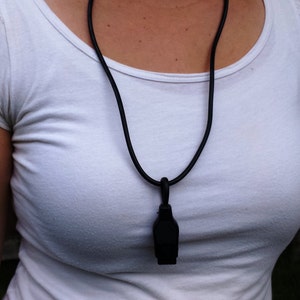 May include: A black pendant necklace with a black cord. The pendant is rectangular and hangs from a black cord. The person is wearing a white t-shirt.