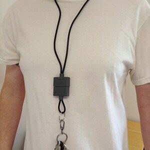 May include: A black lanyard with a gray rectangular key holder and a silver key ring with multiple keys attached.