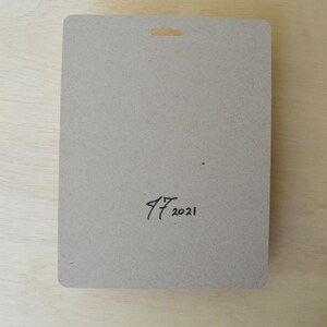 May include: A brown cardboard backing card with a hole at the top for hanging. The card has the handwritten date "17 2021" on the bottom.