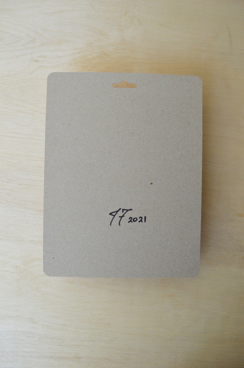 May include: A brown cardboard backing card with a hole at the top for hanging. The card has the handwritten date "17 2021" on the bottom.