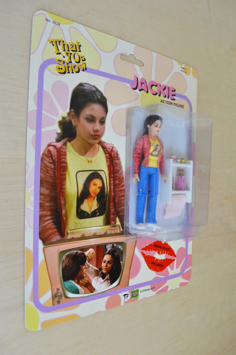 May include: A retro-style action figure of Jackie from the TV show "That '70s Show". The figure is wearing a red jacket, yellow shirt, and blue jeans. The packaging includes a small plastic stand and a makeup kit.