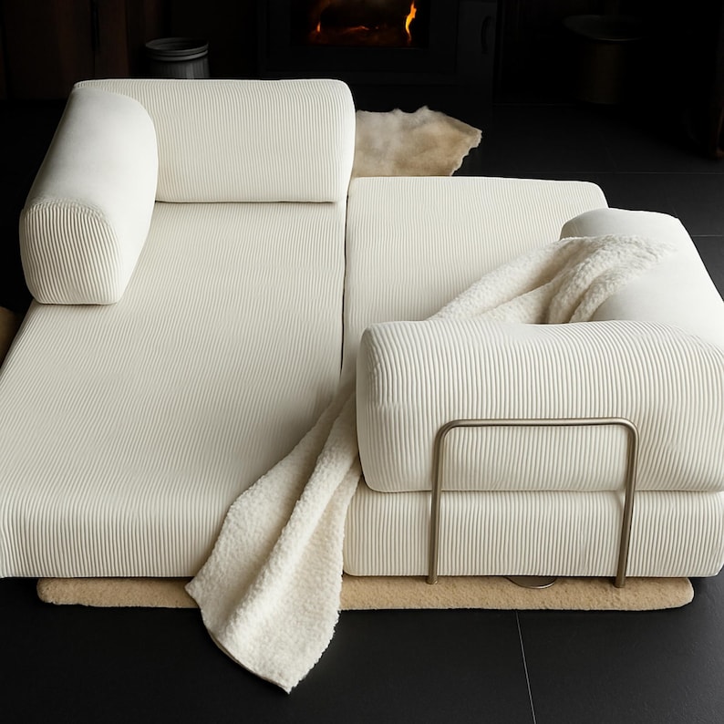 K&ouml;nnte beinhalten: Cremefarbenes Ecksofa mit Cordstruktur. Das Sofa hat abgerundete Armlehnen und R&uuml;ckenkissen. Eine cremefarbene Decke ist &uuml;ber das Sofa drapiert. Das Sofa steht auf einem hellbraunen Teppich.