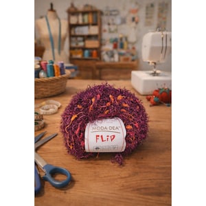Pode incluir: Uma bola de fio Moda Dea Flip em tons de roxo, laranja e rosa está sobre uma superfície de madeira. O fio tem uma aparência texturizada e difusa. Uma etiqueta branca com a palavra "FLIP" está presa ao fio. Tesouras e uma fita métrica também são visíveis.