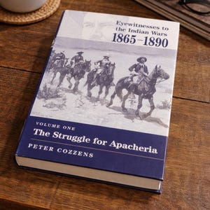 Op de afbeelding: Een hardcover boek getiteld "Eyewitnesses to the Indian Wars 1865-1890" met de ondertitel "The Struggle for Apacheria" door Peter Cozzens. De omslag toont een zwart-wit illustratie van ruiters te paard.