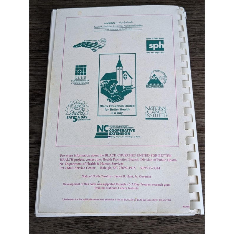 May include: Open book with a white cover and spiral binding. The cover features several logos, including "Black Churches United for Better Health - 5 a Day" and "NC State University Cooperative Extension". The text is in green.