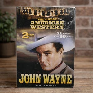 May include: Sealed DVD set titled "The Great American Western" featuring John Wayne. The cover displays a portrait of Wayne in a cowboy hat, with text indicating 11 movies over 10 hours. The set includes 2 DVDs with enhanced audio 5.1.
