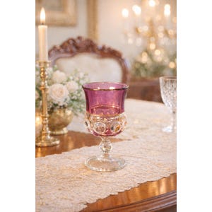 May include: A purple glass goblet with a gold rim and a clear, textured base featuring a pattern of raised circular dots. The stem is faceted and connects to a circular foot, creating a decorative piece of glassware for a table setting.