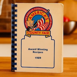 May include: A rustic wooden sign with the text "Welcome" in a handwritten style. The sign is painted white with a distressed finish, and features a decorative floral element in the corner. The background is a blurred image of a wooden surface.