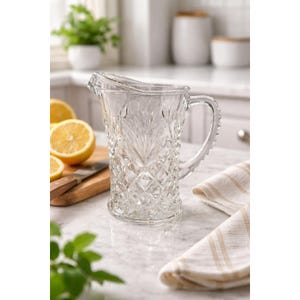 May include: A clear glass pitcher featuring a textured diamond and fan pattern across its exterior surface. The pitcher has a sturdy handle, a wide pouring spout, and a thick base, designed for serving beverages in a kitchen or dining setting.