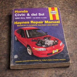 Puede incluir: Un manual de reparación Haynes para modelos Honda Civic & del Sol de 1992-1995. La portada presenta un coche rojo con el capó abierto, mostrando el motor. El título del libro está en texto amarillo y blanco sobre fondo morado.