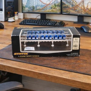 Puede incluir: Un juego de montañas rusas modelo en caja. La caja es negra con la palabra "STATIX" en amarillo y las palabras "by CORSTERDYNAMIX" en blanco. El modelo presenta vagones azules y blancos sobre una pista blanca.