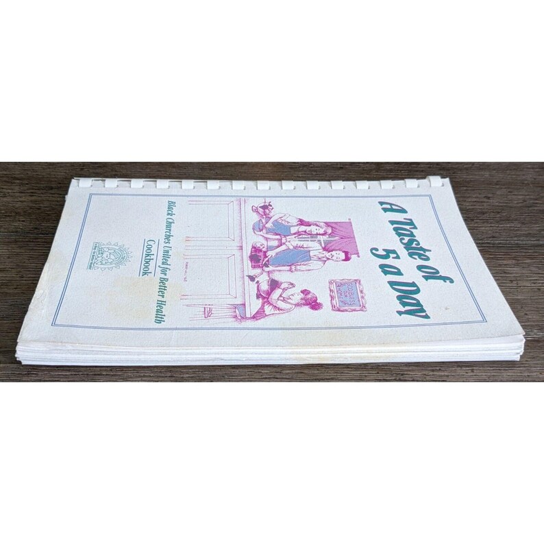 May include: Open cookbook titled "A Taste of 5 a Day" with a spiral binding. The cover features illustrations in pink and blue, with text that reads "Black Churches United for Better Health Cookbook."