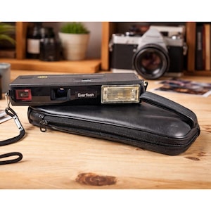 May include: A black Everflash camera with a flash attachment and a black leather case. The camera has a red lens and the text "Everflash" is visible. A second camera is visible in the background.