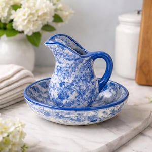 May include: A blue and white ceramic jug and basin set. The jug has a curved handle and spout, and the basin is round. Both pieces feature a speckled pattern. The set is on a marble surface.