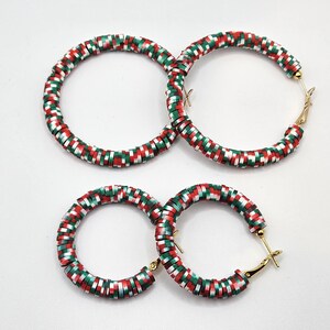 May include: Four hoop earrings with a festive design. The earrings are decorated with red, green, and white accents. The earrings have gold-colored clasps and are set against a white background.