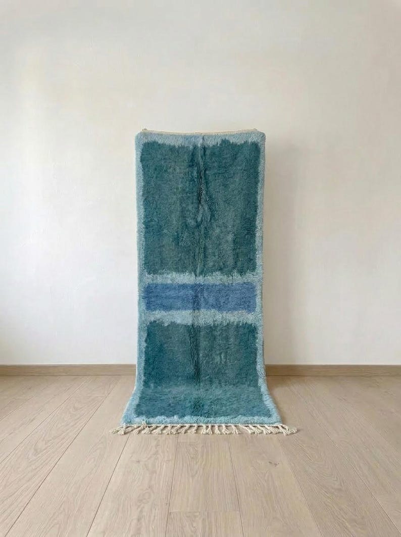 Teal Moroccan wool runner rug with pale blue horizontal bands and fringe on a light studio floor.
