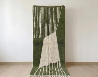 May include: A rectangular area rug featuring a deep olive green and cream colour palette. The design consists of vertical cream stripes on a green background, interrupted by a large, solid cream-coloured geometric shape and cream fringe.