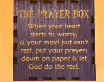 Puede incluir: Una caja de madera cuadrada con el texto "THE PRAYER BOX" en letras doradas. La caja tiene un acabado morado oscuro con un mensaje sobre la oración. La caja tiene un borde decorativo.