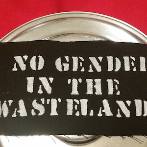May include: Black fabric patch with white text that reads "NO GENDER IN THE WASTELAND!"