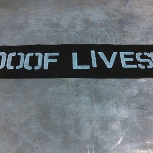 May include: A black rectangular sign with white lettering that reads "100 OF LIVES!"