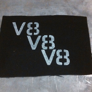 Puede incluir: Parche de tela negro con el texto "V83" repetido tres veces en un patrón escalonado, con cada instancia del texto ligeramente más pequeña que la de arriba.