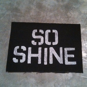 Puede incluir: Parche de tela negro con texto bordado en blanco que dice "SO SHINE".
