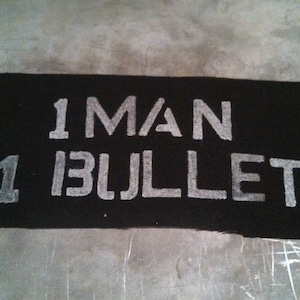 Könnte beinhalten: Schwarze Fußmatte mit weißem Text, der "1 MAN 1 BULLET" lautet.
