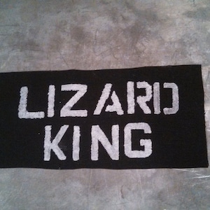 Puede incluir: Pancarta de tela negra con texto blanco que dice "Lizard King".