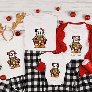 May include: A family Christmas pyjama set. White tops with a cartoon character in a Santa hat and patchwork design. Includes a onesie, t-shirts, and a long-sleeved shirt, paired with black and white plaid trousers. Festive holiday decor.