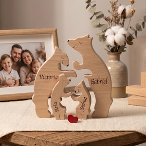 May include: Wooden family bear puzzle with the names Victoria, Gabriel, Aria, and Joshua engraved. A small red heart sits at the base. A framed family photo and a vase of dried flowers are in the background.