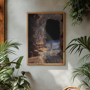 Pode incluir: Uma impressão artística emoldurada retrata uma figura em pé na entrada de uma caverna, olhando para um planeta distante. A obra de arte apresenta uma paleta de cores quentes com tons de castanho, azul e dourado. A impressão é exibida em uma parede cinza, rodeada por plantas verdes.