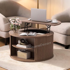 May include: A brown lift-top coffee table with a laptop, mouse, and coffee cup on top. The table has a round base with vertical wood paneling and open storage shelves. A speaker and books are on the shelves. The text "ElegantHomeDecorr" is visible.
