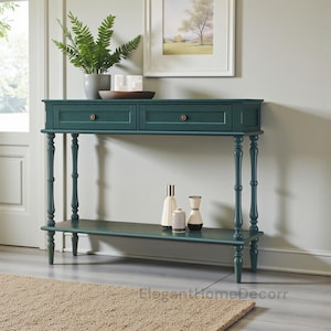 May include: Teal console table with two drawers and a lower shelf. The table has turned legs and brass-colored knobs. Decorative items, including vases and a potted fern, are displayed on the table. The table is approximately 48 inches long.