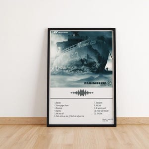 May include: A framed poster featuring a grayscale image of a ship breaking through icy waters. The poster includes the band name "Rammstein" and a tracklist. The poster is in a black frame and is displayed on a wooden floor.