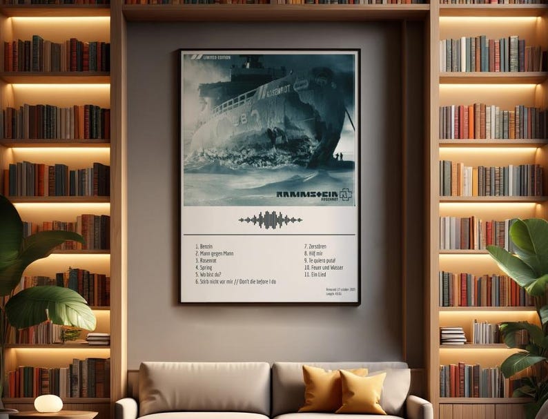May include: A framed poster featuring a grayscale image of a ship at sea, with the band name and a list of song titles below. The poster is displayed on a neutral wall between two bookshelves filled with books. A sofa with yellow pillows sits below.