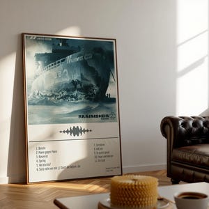 May include: A framed poster featuring a distressed image of a ship, with the band name "Rammstein" and a tracklist. The poster has a beige background and a wooden frame. The image is in shades of blue and gray, with the text "Limited Edition" at the top.