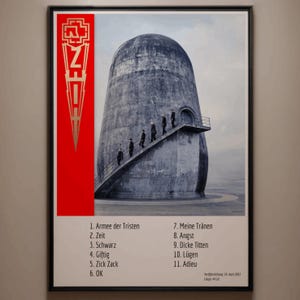 May include: Framed poster featuring a band's logo in gold and a red vertical stripe. The image shows a concrete structure with a staircase, and figures ascending. The poster includes a list of song titles in German.