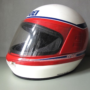Peut inclure: Casque de moto blanc, rouge et bleu avec une visière transparente. Le casque porte l'inscription "SHOEI" et le texte "TF280". Conçu pour la sécurité et la protection du motard.
