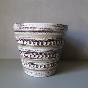 Può includere: Un vaso di ceramica con un design a righe strutturato. Il vaso presenta fasce bianche, marroni e verde chiaro. Le fasce marroni hanno un motivo a pois. Adatto per uso interno o esterno.