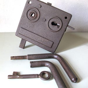 Puede incluir: Un mecanismo de cerradura de sobreponer de hierro fundido texturizado en color marrón oscuro con un orificio cuadrado para el cuadradillo y una bocallave. Incluye dos manillas metálicas en forma de L y una llave con acabado oxidado.